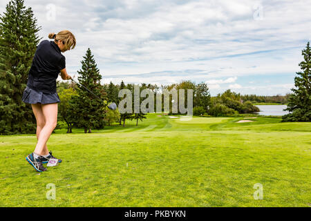 Un giocatore di golf femminile abilmente alla guida di una pallina da golf all'erba verde di un campo da golf con la palla a metà aria; Edmonton, Alberta, Canada Foto Stock