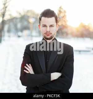 Bel giovane uomo con la barba che indossa un abito nero su un tramonto Foto Stock