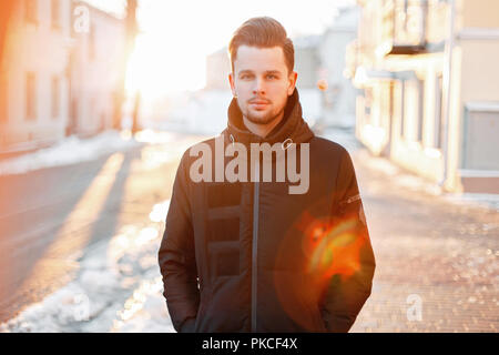 Bel giovane con capelli stile in una giacca nera a camminare sulla strada al tramonto Foto Stock