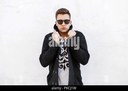 Giovane uomo bello in occhiali da sole e un maglione su uno sfondo bianco. Foto Stock
