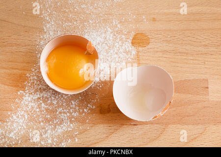 La cucina e il forno sfondo con close up di uova rotte, tuorlo d'uovo in guscio d'uovo, la farina su uno sfondo di legno Foto Stock