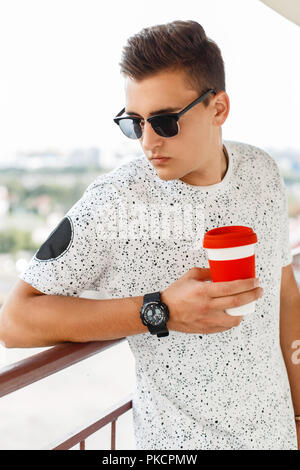 Bello ed elegante hipster Uomo con occhiali da sole tenendo una tazza di caffè Foto Stock
