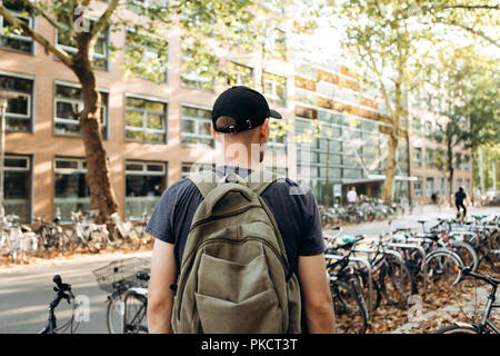 Uno studente con uno zaino o un turista su strada di Lipsia in Germania nei pressi del parcheggio per biciclette che si trova accanto alla biblioteca dell'Università di Leipig e ostello della gioventù. Foto Stock