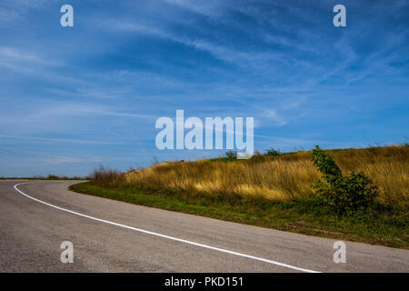 Svuotare strada asfaltata oltre il campo di erba durante l'estate Foto Stock