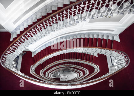 La simmetria di architettura con eleganti scale a spirale, sopra vista, realizzato in marmo bianco e ricoperta con moquette rossa e in un albergo a Genova, Italia. Foto Stock