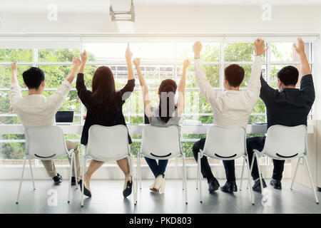 Per celebrare il successo. Un gruppo di giovani uomini di affari in aumento le mani e cercando felice seduti ai loro posti di lavoro in ufficio Foto Stock