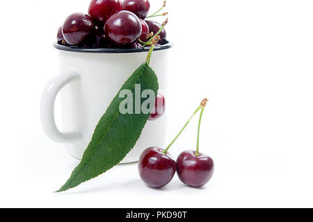 Tazza bianca con bacche mature di Rosso ciliegio dolce e diverse bacche nella parte anteriore della tazza. Composizione su uno sfondo bianco. Foto Stock