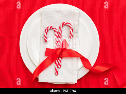 Tavola di natale l'impostazione. Candy canes su piastre bianche e igienico, rosso tovaglia, vista dall'alto Foto Stock