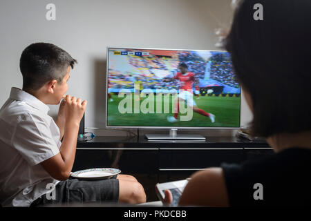 Scolaro 10 anni,nell'uniforme scolastica snacking e guardare la partita di calcio in TV Foto Stock