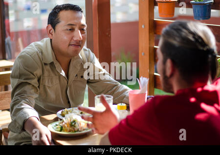 Guardando bene gli uomini a pranzo in un ristorante all'aperto, gli uomini in chat e sorridente Foto Stock