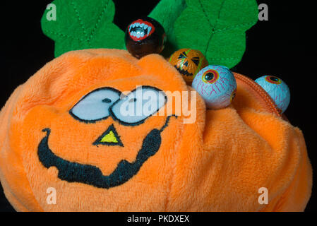 Divertente il giocattolo di peluche a forma di zucca di Halloween con i lotti delle sfere di cioccolato intorno ad esso, coperto con un bel smile, su uno sfondo nero. Utilizzare Foto Stock