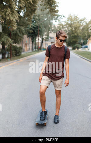 Giovane ragazzo bello in occhiali da sole a cavallo su uno skateboard. Foto Stock