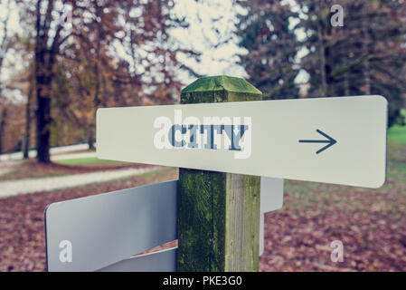 Città cartello con la freccia rivolta verso destra e testo su un rustico di palo di legno nel bosco con un sbiadito effetto retrò. Foto Stock