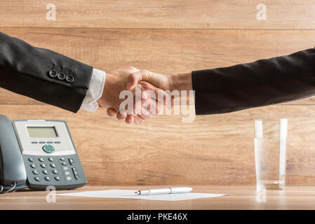 Stretta di mano del due business partner dopo un meeting di successo presso l'ufficio, al di sopra di un contratto firmato, collocato sulla scrivania in legno, vicino al telefono. Foto Stock