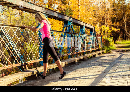 Un attraente donna di mezza età delle pause di riposo su un ponte durante una corsa su un bellissimo autunno caldo la sera in un parco della città; Edmonton, Alberta, Canada Foto Stock