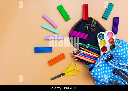 Forniture scolastiche cadono fuori di zaino su sfondo beige. Vista dall'alto. Foto Stock