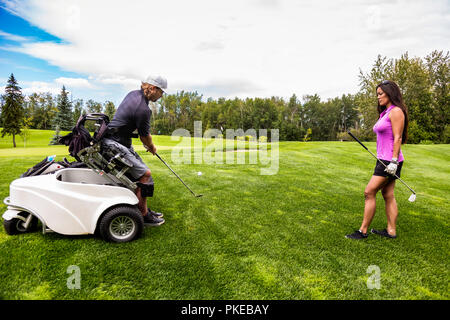 Un golfer fisicamente disabilitato, usando una sedia a rotelle specializzata, colpisce la sfera di golf con il suo randello di golf sul verde di golf come... Foto Stock