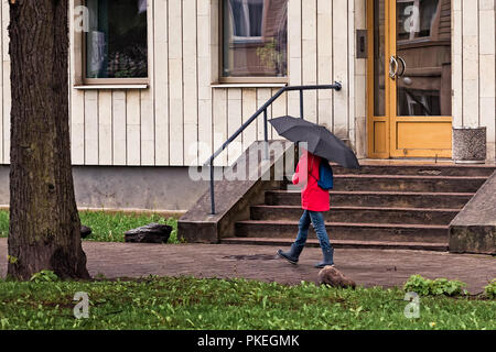 Un bambino a piedi con un grande ombrellone e un rosso cappotto di pioggia in un giorno di primavera a Tallinn in Estonia. Foto Stock