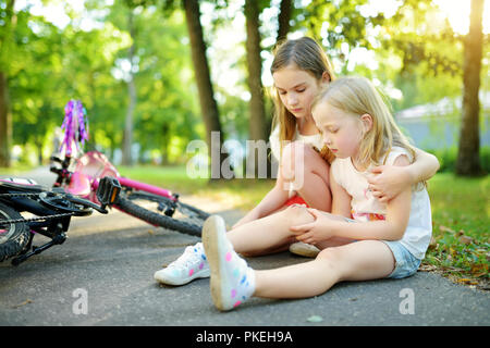 Adorabile ragazza consolante la sua sorellina dopo che lei è caduto il suo moto in estate park. Bambino di farsi male mentre in sella ad una bicicletta. Famiglia attiva leisur Foto Stock