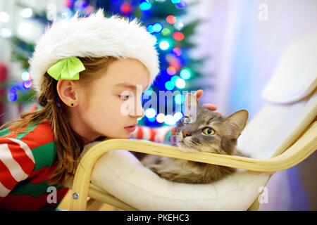 Adorabile bambina di accarezzare il suo gatto il giorno di Natale. Trascorrere il tempo con la famiglia e gli animali domestici a Natale. Celebrare il Natale a casa. Foto Stock