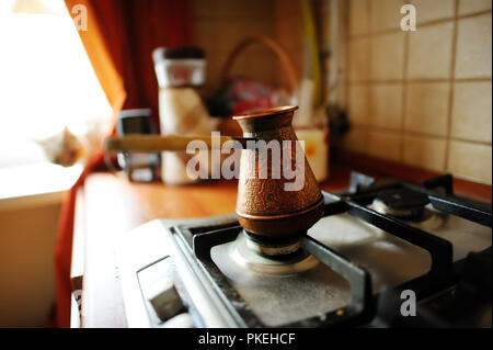 Caffè servito in un cezve di rame su una stufa a gas in accogliente cucina al mattino. La preparazione di un caffè delizioso in cezve. Foto Stock