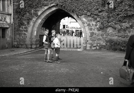 Degli anni Cinquanta, storico, Colonia, Germania, tre ragazzi indossando il tradizionale tedesco pantaloncini in pelle o lederhosen, assieme al di fuori di un ingresso ad arco al centro storico della città. Foto Stock