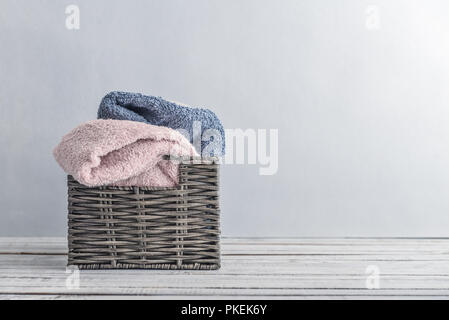 Asciugamani da bagno di colori diversi nel cesto in vimini su sfondo chiaro Foto Stock