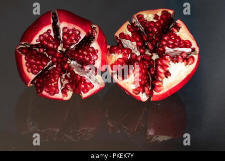 Due sani e succosa aperto melagrane in appoggio sul riflettente la superficie di vetro Foto Stock