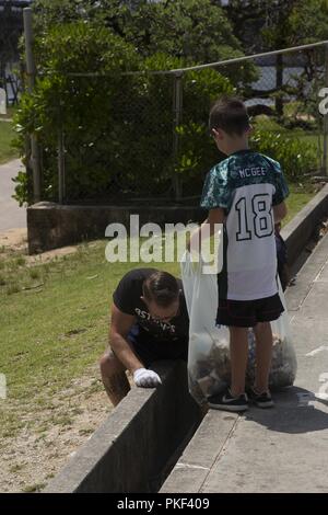 CHATAN, Okinawa, Giappone - padre e figlio raccoglie la spazzatura durante una giornata di amicizia beach cleanup 4 agosto sulla spiaggia al tramonto sul mare in parete Chatan, Okinawa, in Giappone. Quattro team da parte degli Stati Uniti Le forze del Giappone - American Football League ha trascorso la giornata per ripulire il cestino in tutto il seawall e ci siamo goduti un cookout dopo. La pulizia consente ai giocatori e famiglia da tutte le squadre di trascorrere del tempo insieme fuori dal campo di calcio e di lavorare insieme per prendersi cura della loro comunità. Foto Stock