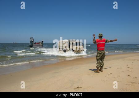 VIRGINIA BEACH, Va. (26 luglio 2018) un marinaio da unità Beachmaster (BMU) 2 guide un U.S. Esercito il veicolo su Utah Beach dopo la partenza da un assalto unità artigianali (ACU) 2 Landing Craft Utility (LCU) 1600 onboard Expeditionary Comune Base Little Creek - Fort Story durante il Tridente Sun 18 esercizio. Trident Sun 18 è un preposizionamento marittima forza (MPF) operazione destinata a fornire una formazione alla componente di riserva personale per quanto riguarda il flusso in offload di veicoli e attrezzature militari. Foto Stock