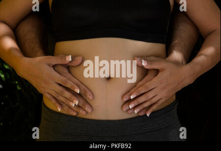 Giovane tenendo le mani sulle donne incinte pancia Foto Stock