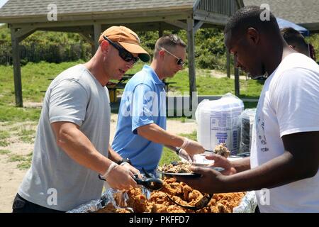 Sgt. Il Mag. Christopher Davis, sinistra, serve cibo di un Marine durante la sede e Sede squadrone Beach Bash a Fort Macon, N.C., 10 Agosto, 2018. I partecipanti sono stati forniti gratuitamente il cibo e la possibilità di partecipare a numerose attività tra cui pallavolo, beanbag toss e nuoto. Oltre 230 marines e loro familiari hanno partecipato a questo anno la spiaggia Bash. Foto Stock