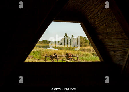 Giorno di estate in agriturismo con lo stagno e i vecchi macchinari; guardare attraverso il fienile Foto Stock