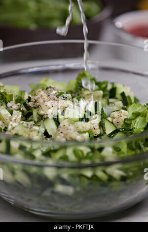 Spruzzata di succo di limone su una nutriente insalata verde con cetrioli, nocciole e cipolline in recipiente di vetro, close up Foto Stock