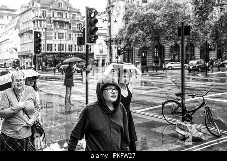 24 Agosto 2018 - Londra, Inghilterra. Immagine in bianco e nero di un gruppo di persone intrappolate in cattive condizioni atmosferiche. Una donna che copre con grande vecchio libro da Foto Stock