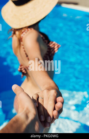 Ritagliato shot di man mano tesa della giovane moglie in piscina, follow me concetto Foto Stock