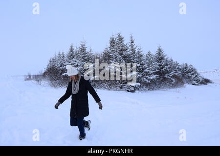 Donna vedendo la neve per la prima volta la calciata neve in campo con alberi Foto Stock