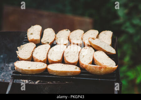 Molte fette di baguette tostate il pane su una griglia sopra il fuoco su aria fresca Foto Stock