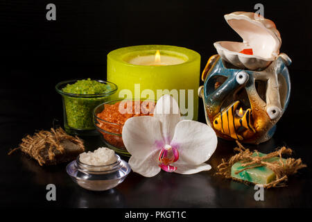 Prodotti per il benessere con white orchid fiore, sapone artigianale, bocce con sale marino, candele su sfondo nero Foto Stock