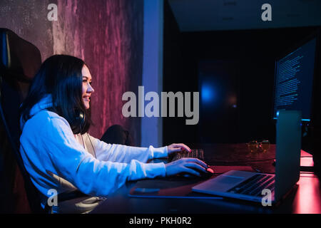 Allegro giovane donna freelancer in abbigliamento casual digitando il codice di programmazione lavoro sul laptop moderno computer a casa. Studente positivo aggiornamento software su netbook Foto Stock