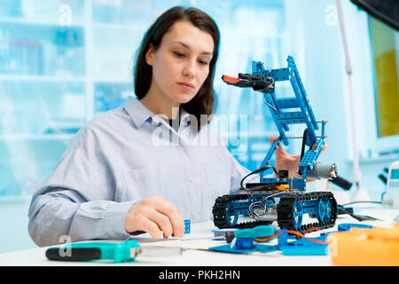 Ragazza dello studente nel laboratorio di elettronica, esperimento con microcontrollore e robot modulo cnc Foto Stock