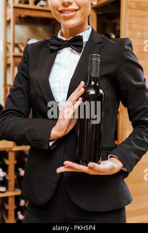 Ritagliato shot femminile di sommelier tenendo la bottiglia a wine store Foto Stock