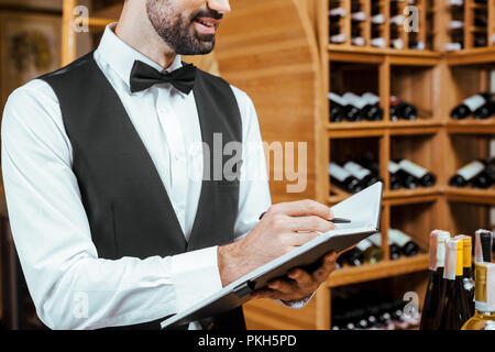 Ritagliato shot di sorridere giovani sommelier rendendo note al negozio dei vini Foto Stock