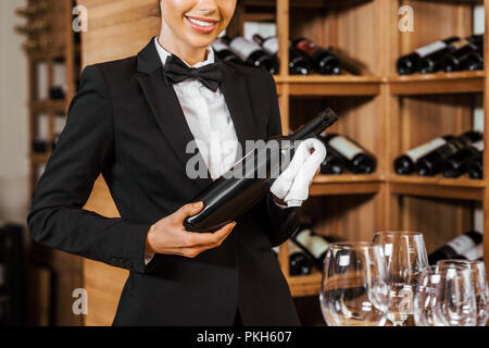Ritagliato colpo di donna sorridente sommelier tenendo la bottiglia a wine store Foto Stock