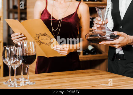 Ritagliato colpo di sommelier azienda decanter mentre client nel menu lettura elenco presso il negozio dei vini Foto Stock