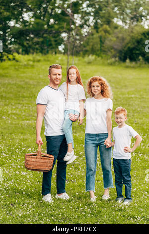 La famiglia felice sorridente alla telecamera mentre in piedi con Cesto picnic nel parco Foto Stock