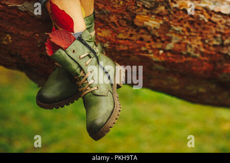 Verde stivali in pelle sulle donne gambe decorate con caduta di fogliame di autunno di foglie di albero marrone dello sfondo. Progettazione di scarpe, concetto, Pubblicità. Foto Stock