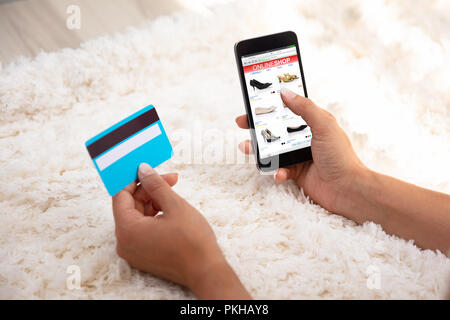 Donna di mano utilizzando la carta di credito per gli acquisti online sul cellulare su un tappeto Foto Stock