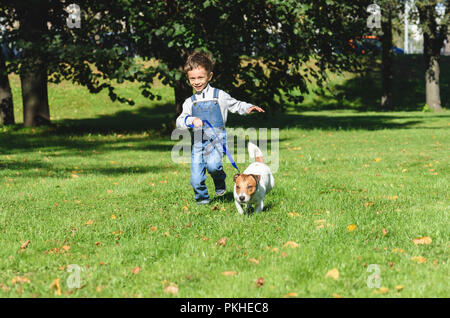 Kid boy in esecuzione con il cane al guinzaglio al parco Prato Foto Stock