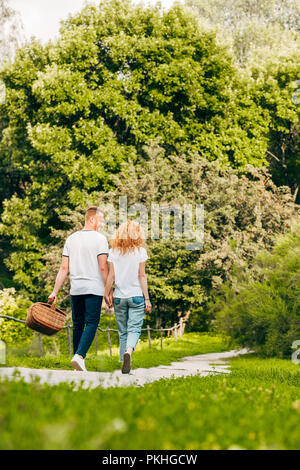 Vista posteriore della coppia giovane con Cesto picnic passeggiando nel bellissimo parco Foto Stock